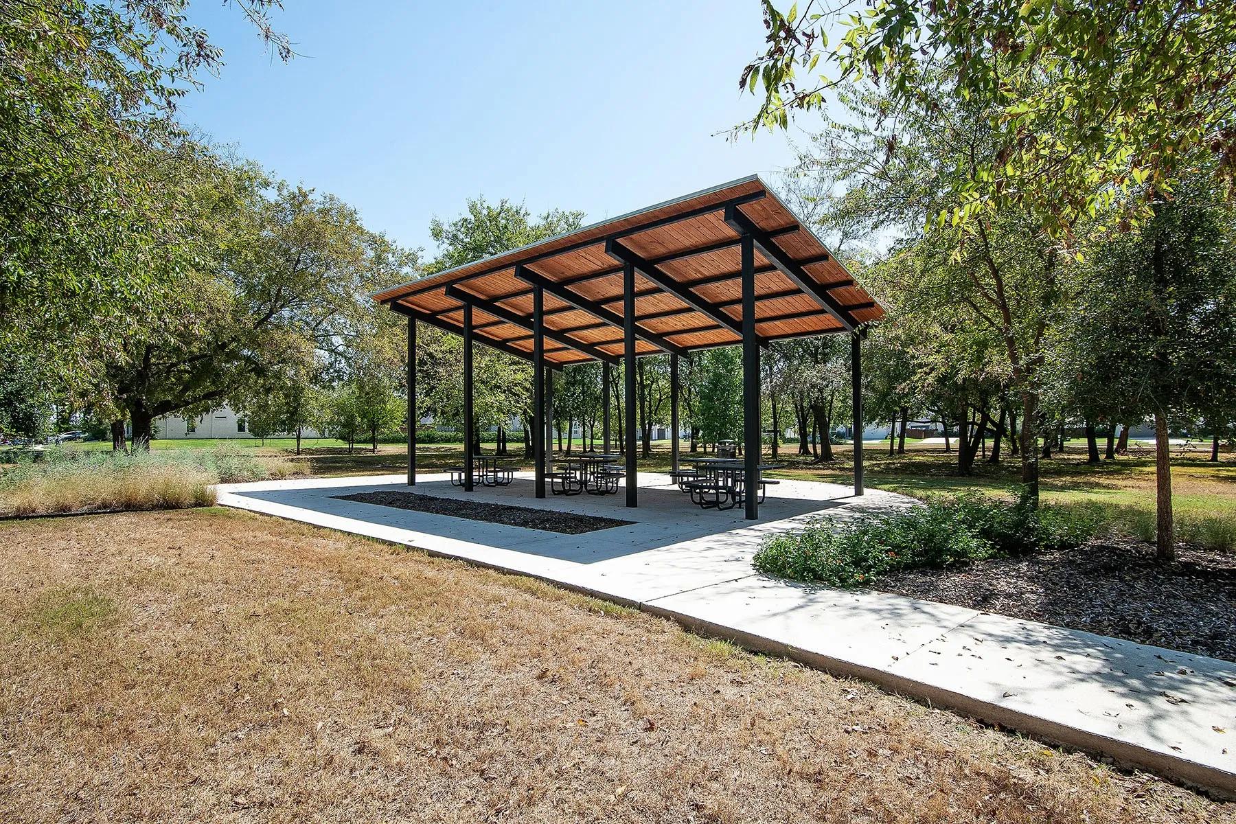 Covered pavilion with a pitched roof, concrete flooring, and surrounding mature trees