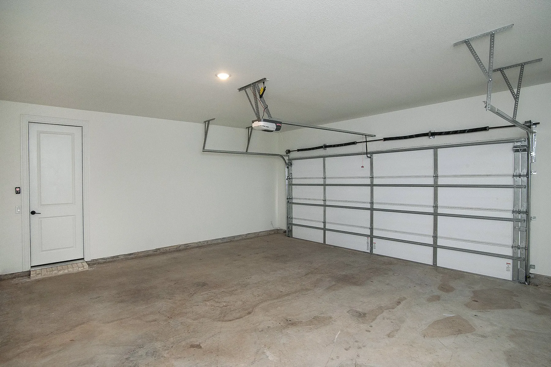 Spacious 2.5 car garage with an overhead door, concrete flooring, recessed lighting, and a white panel door