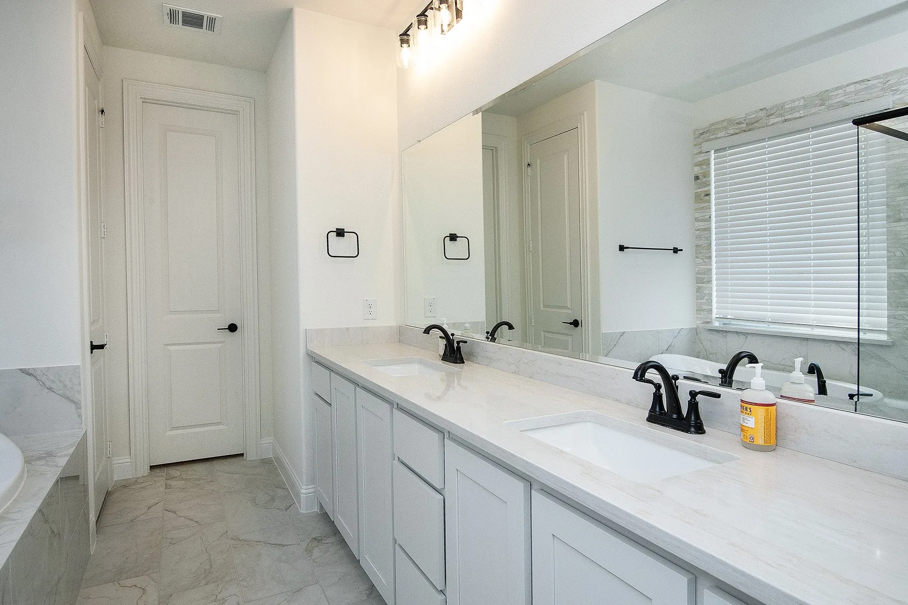 Dual vanity with integrated sinks, light-toned countertops, matte black fixtures, full-width mirror, and tiled flooring