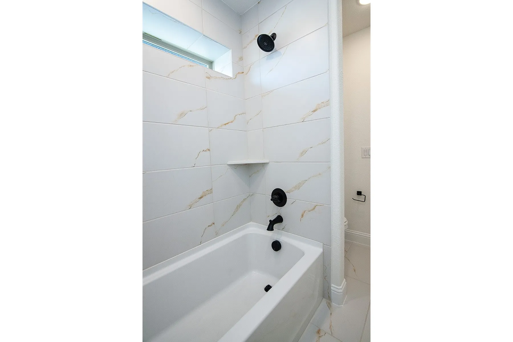 Bathtub with white subway tile surround, matte black fixtures, and a built-in shower niche