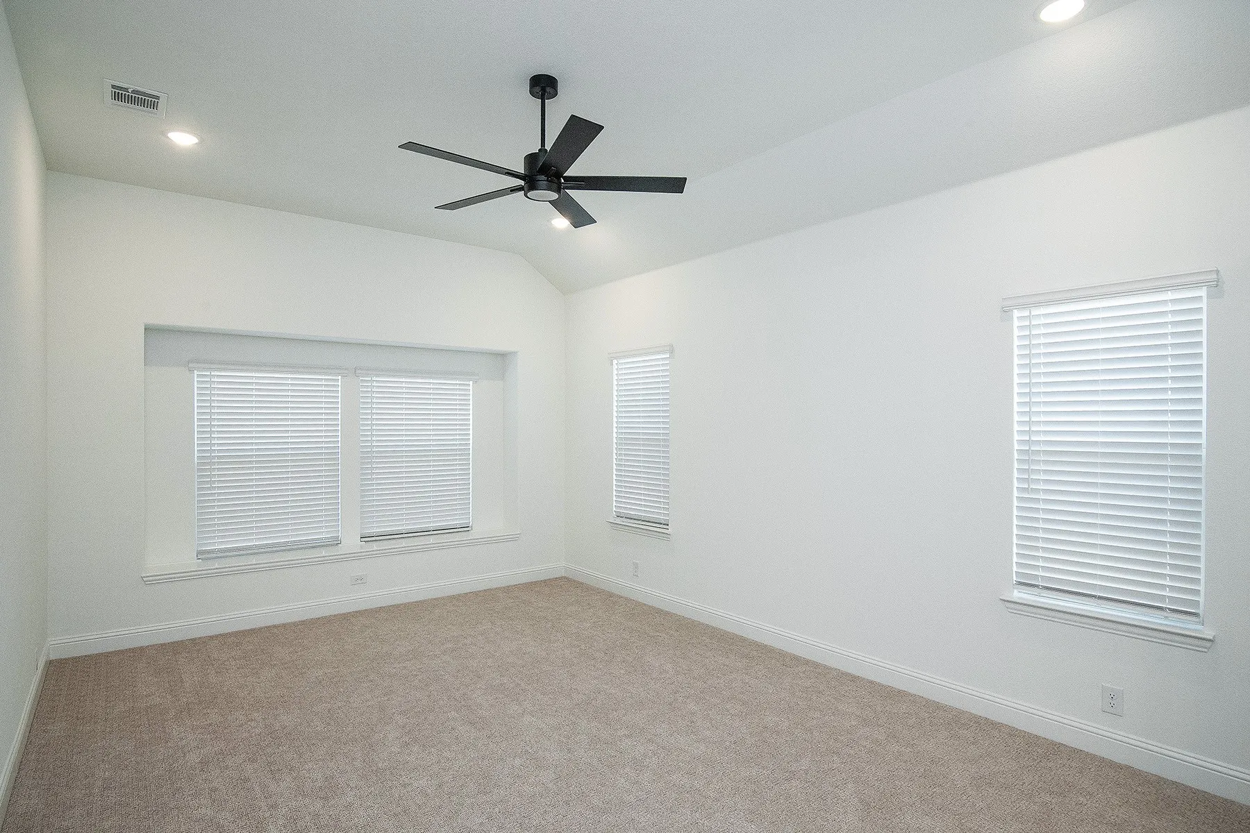Vaulted ceiling with recessed lighting, black ceiling fan, multiple windows with blinds, and neutral carpet flooring