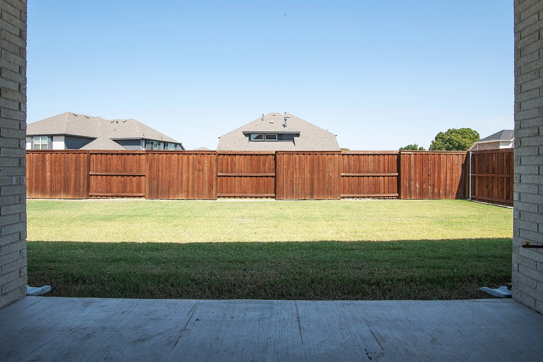 Expansive backyard with a large grassy area, wooden privacy fencing, and concrete patio