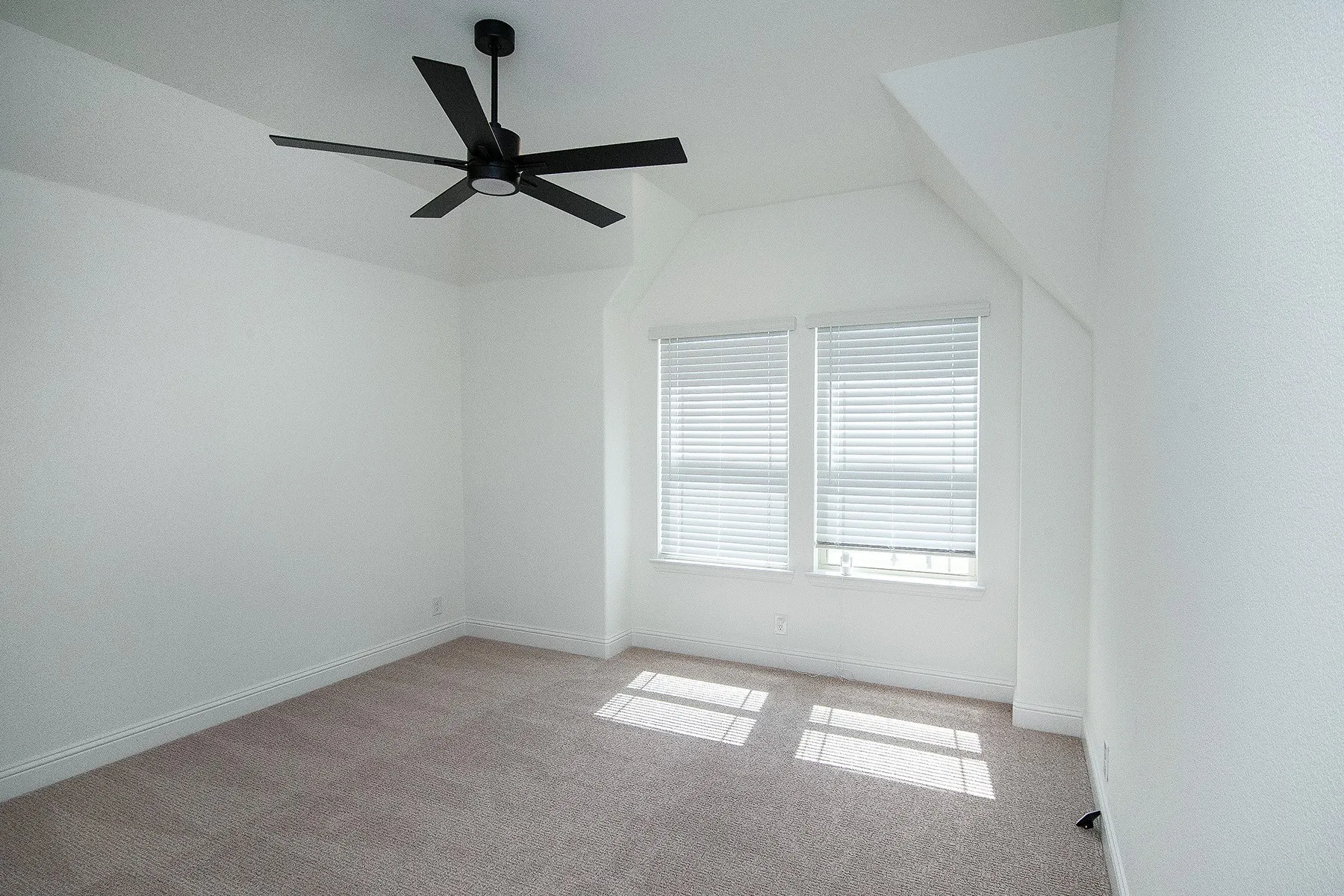 Carpeted room with a modern ceiling fan, dual windows, and sloped ceiling details