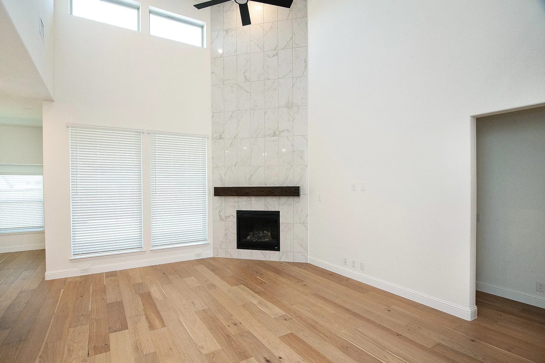 Sleek fireplace with stone-look surround, wood-finish mantel, and elevated ceilings