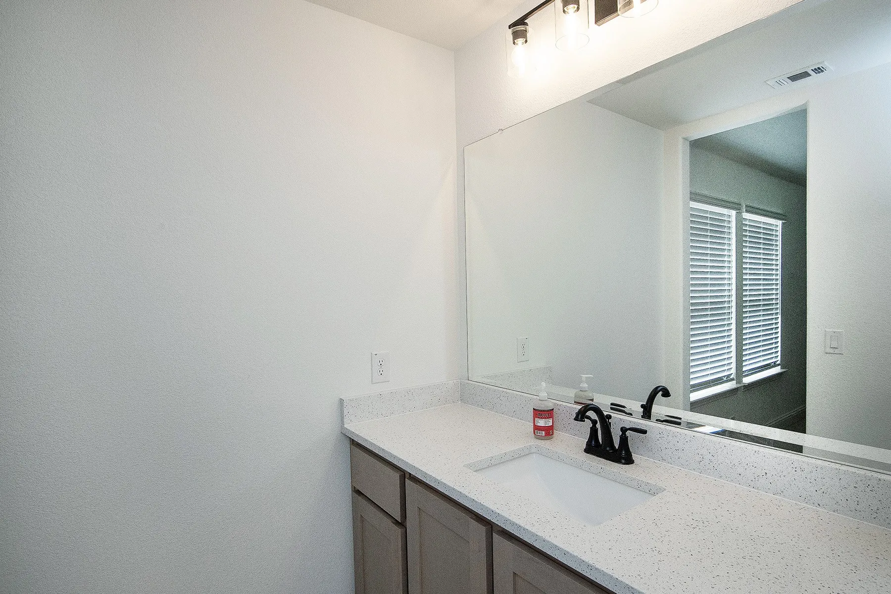 Vanity with a light-toned countertop, integrated rectangular sink, and matte black faucet