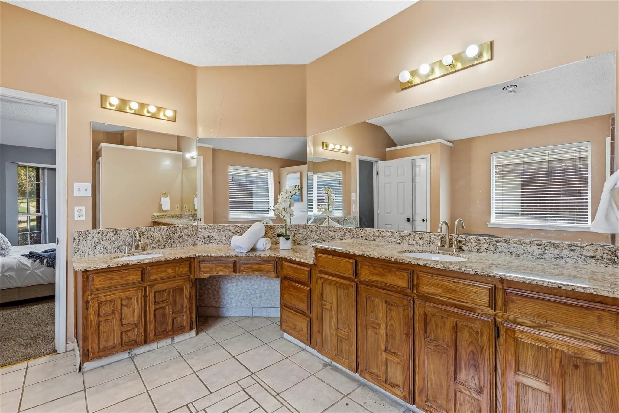 Dual vanity with stone countertops, wood cabinetry, integrated sinks, large mirrors, and tile flooring