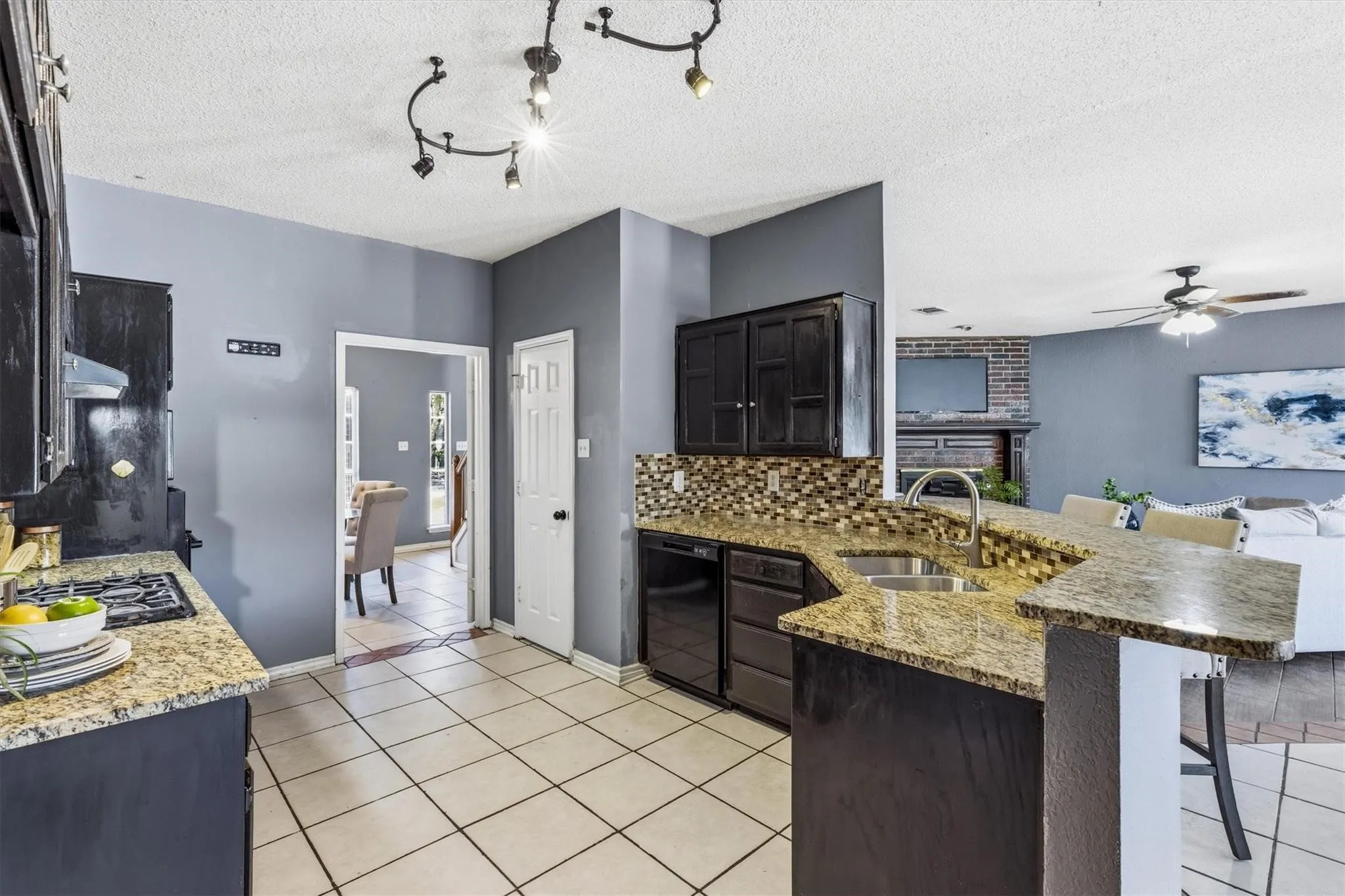Kitchen featuring granite countertops, tile flooring, dark wood-finish cabinetry, a tile backsplash, and a double basin sink
