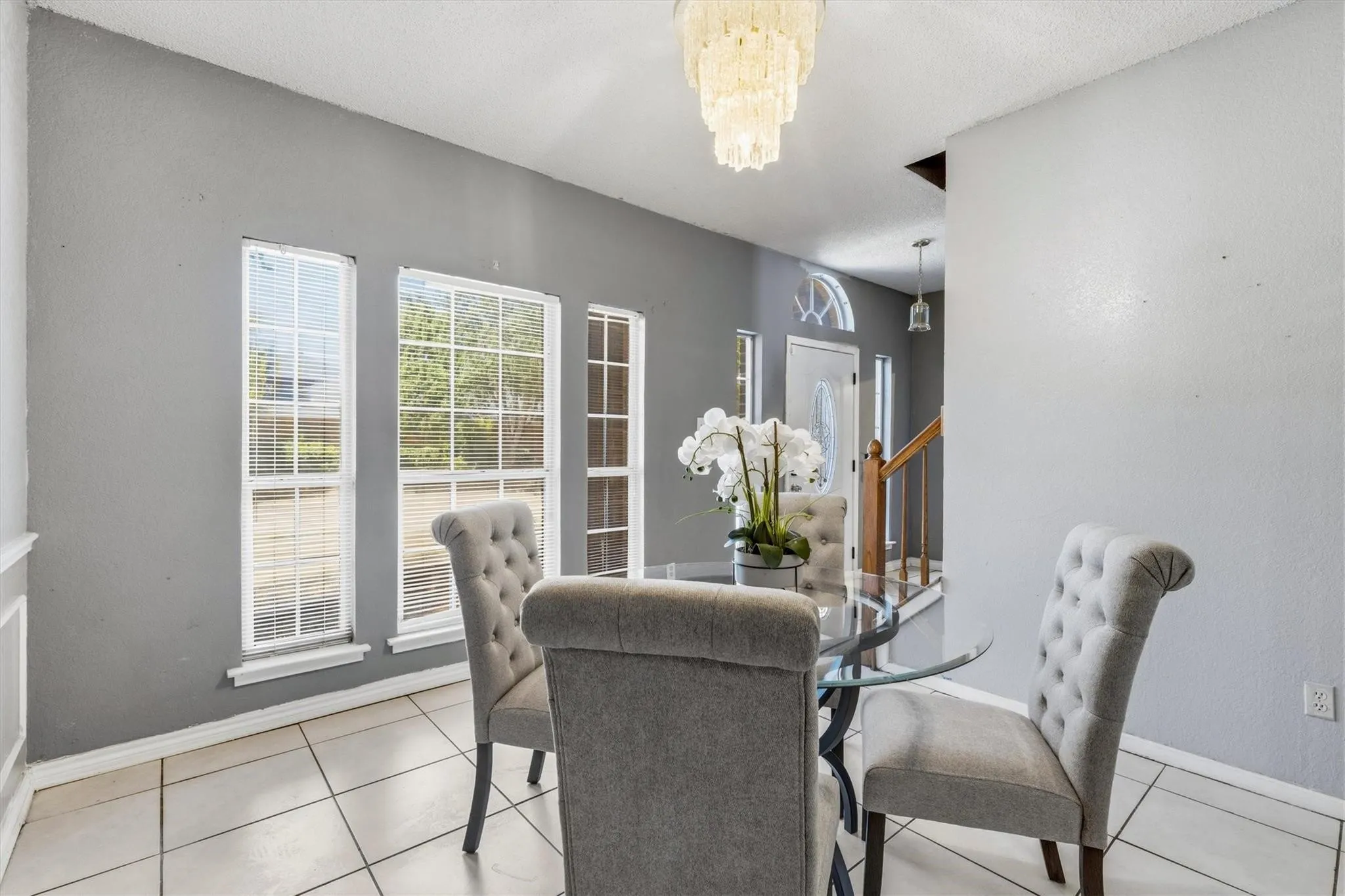 Tile flooring, multiple windows, a chandelier light fixture, and a staircase with wood railing