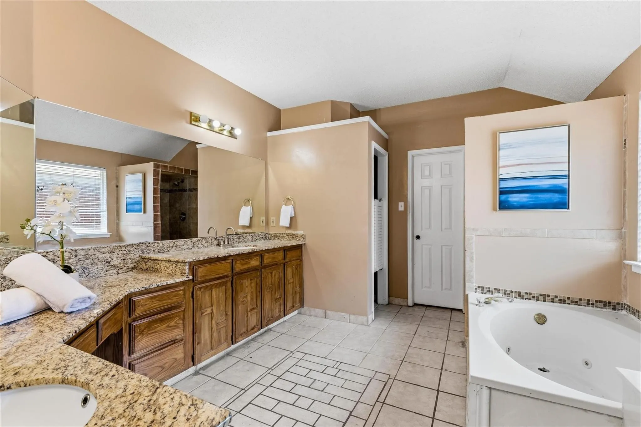 Spacious bathroom featuring a dual vanity with granite-style countertops, an integrated soaking tub with tile surround, a separate shower enclosure with glass paneling, and ceramic tile flooring