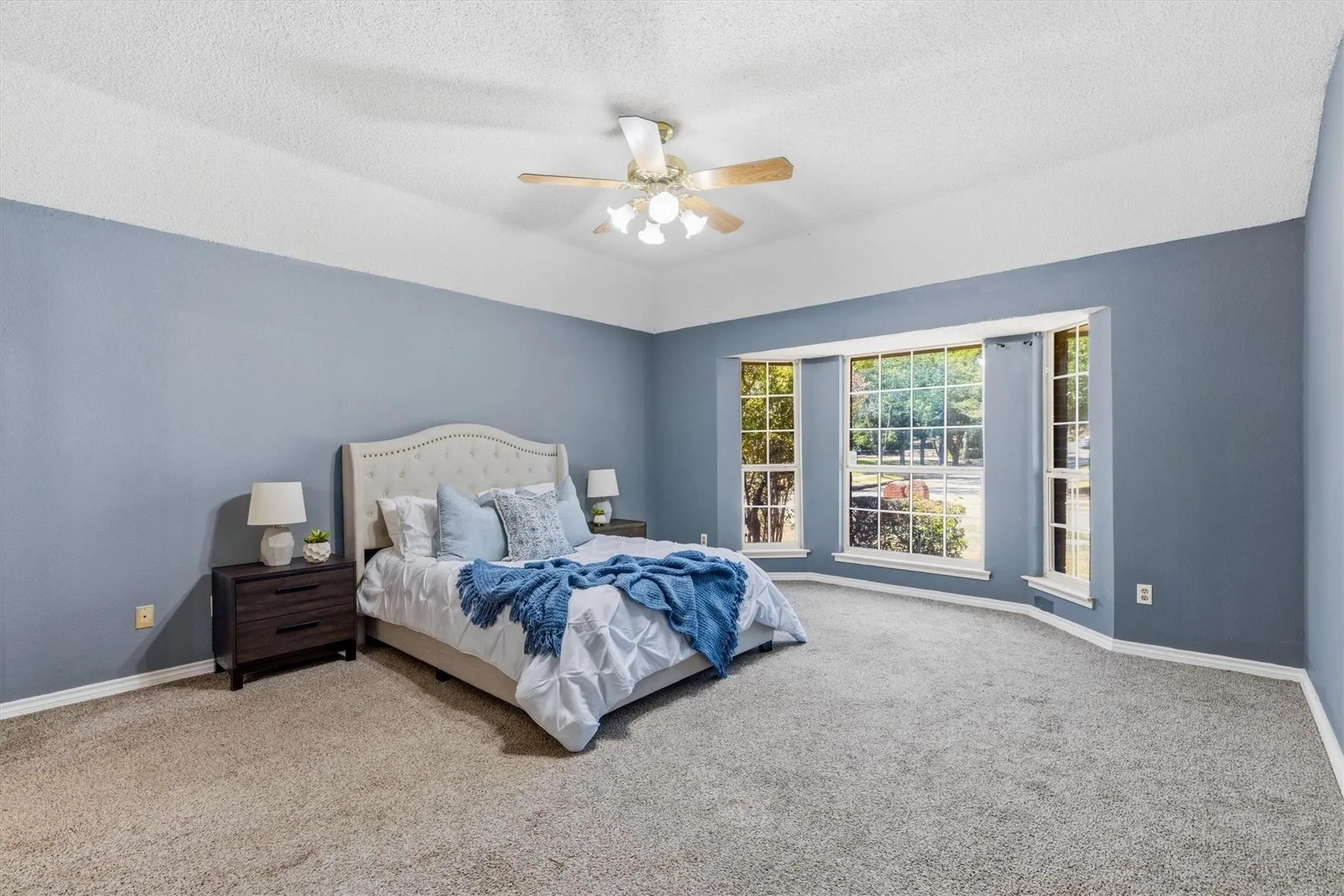 Vaulted ceiling with a ceiling fan, bay window, carpeted flooring, and light blue wall finish