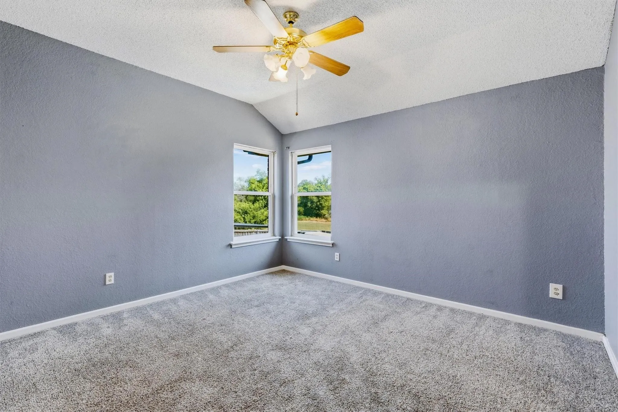 Vaulted ceiling with a ceiling fan, dual windows, and wall-to-wall carpeting