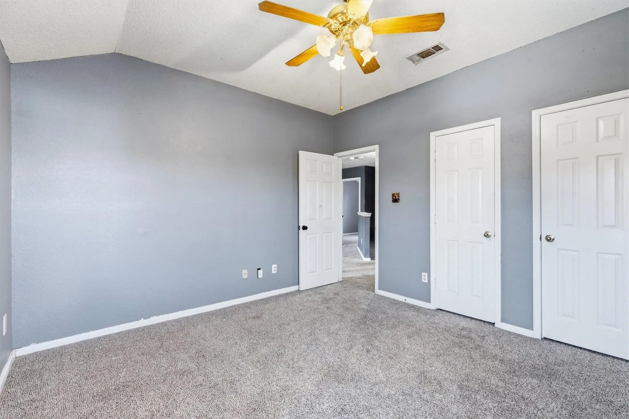 Vaulted ceiling, ceiling fan with light fixture, gray carpet, two paneled doors, gray painted walls