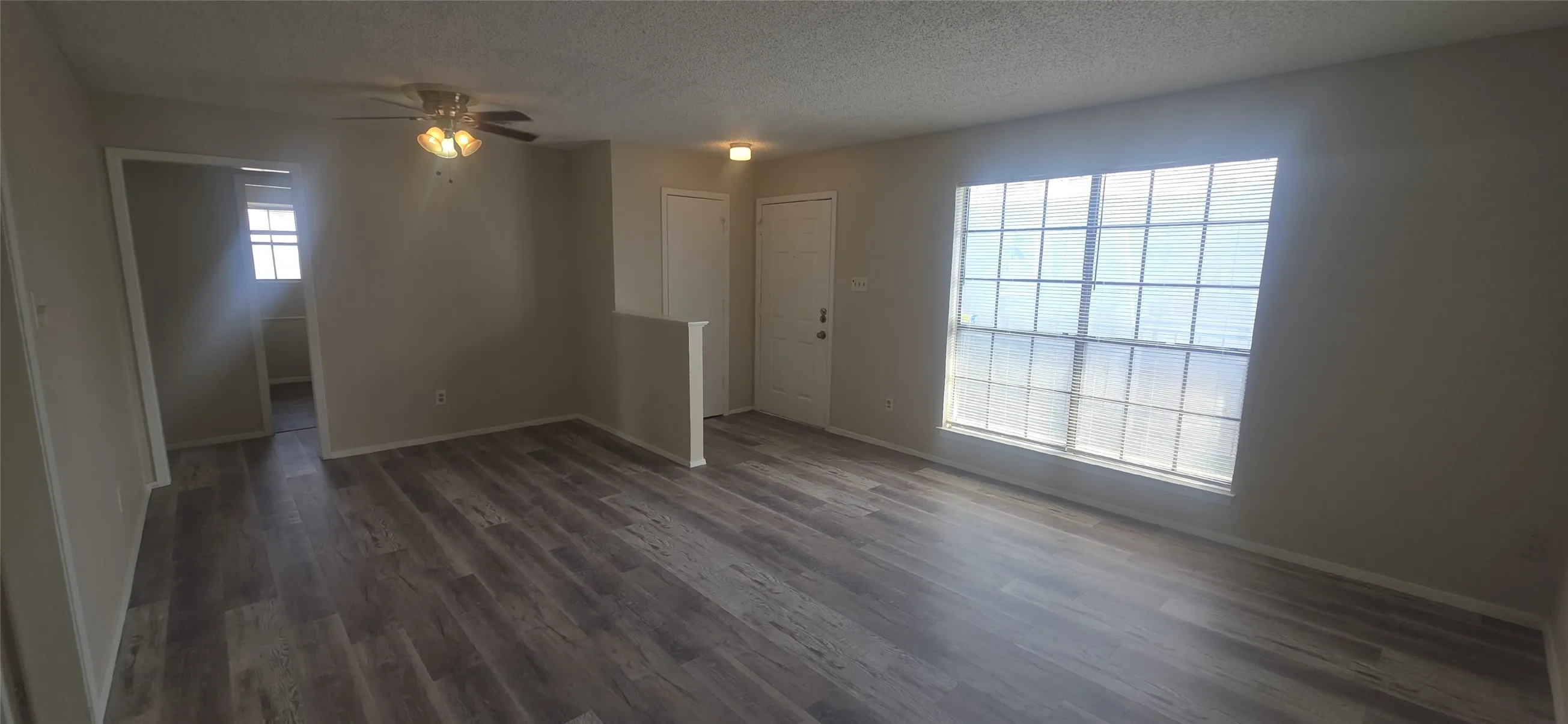 Spacious room featuring wood-finish flooring, a large multi-pane window, and neutral wall tones