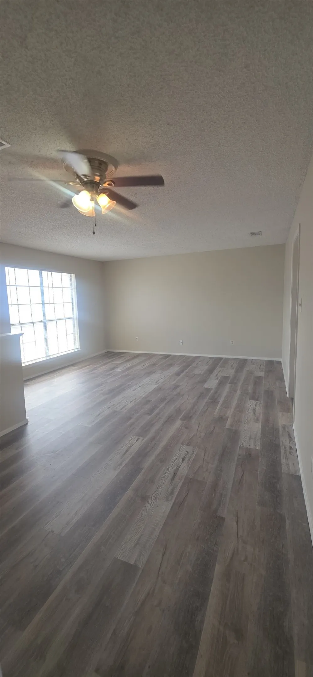 Wood-finish flooring, neutral wall tones, multi-light ceiling fan, and a large window