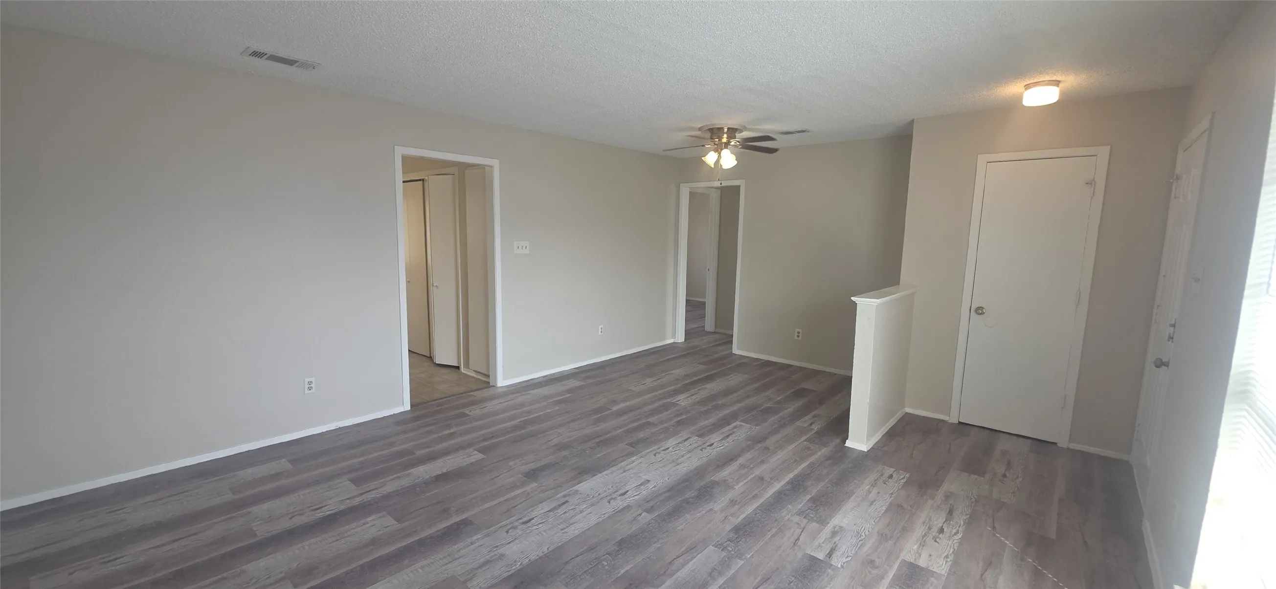 Spacious interior featuring wood-finish flooring, light neutral wall tones, multiple doorways, and a ceiling fan