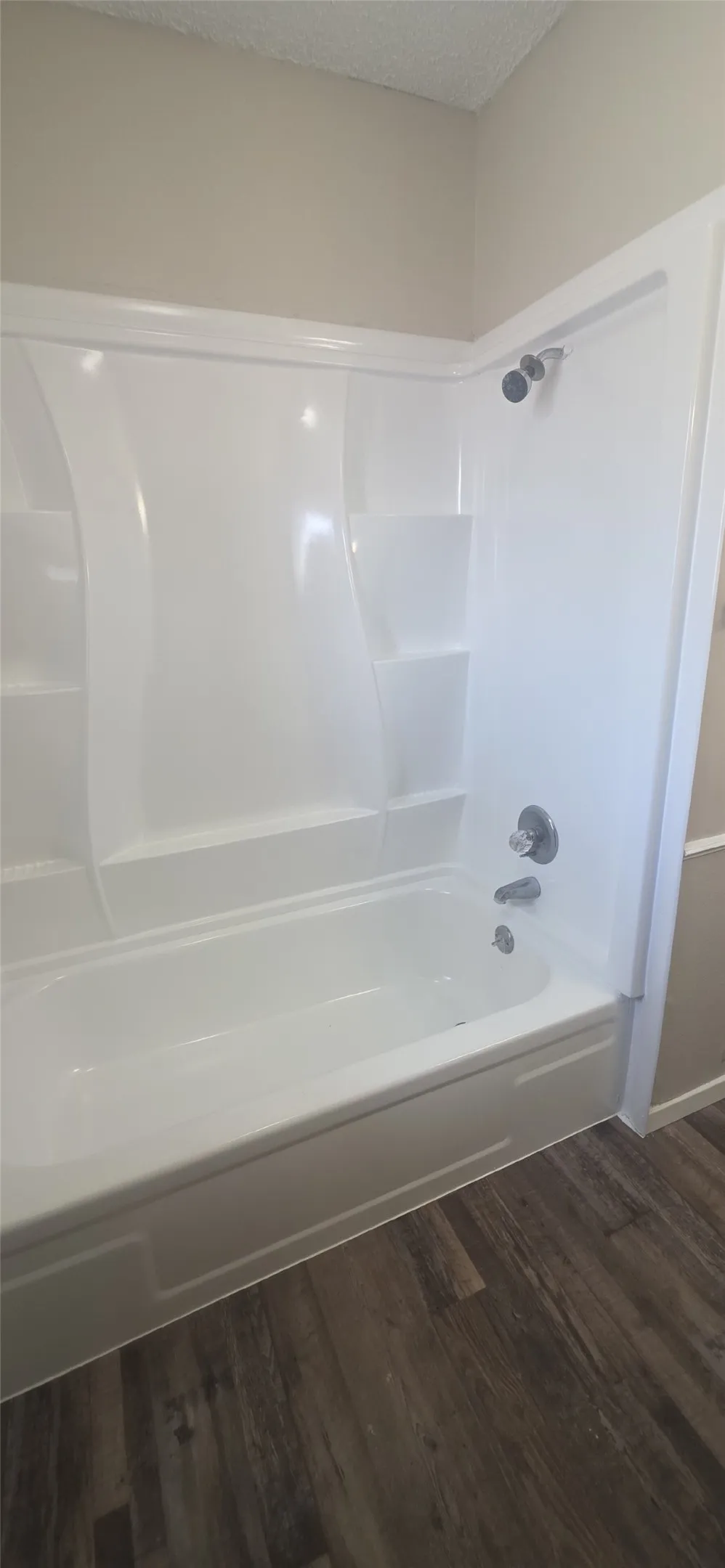 White shower/tub combination with integrated shelving, chrome fixtures, and wood-finish flooring