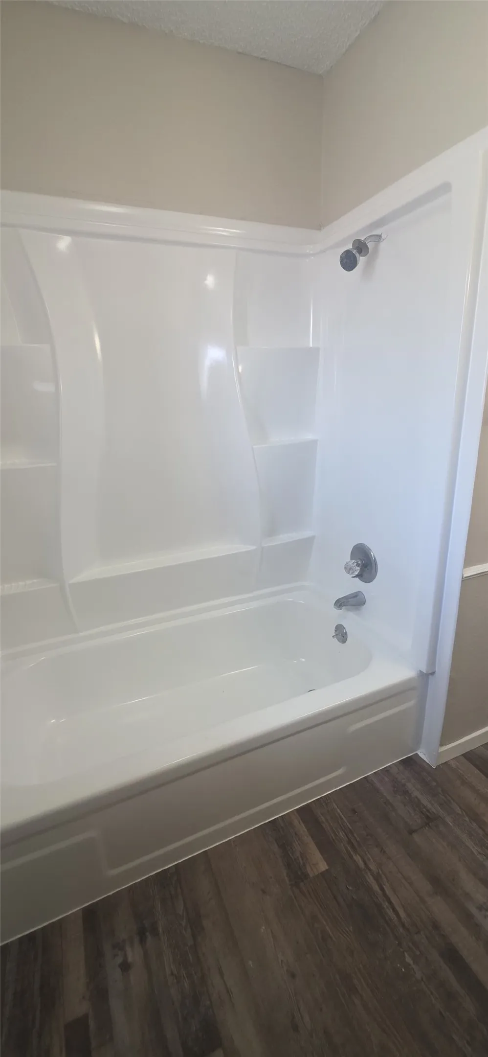 Bathtub and shower combination with integrated shelving, chrome fixtures, and wood-finish flooring