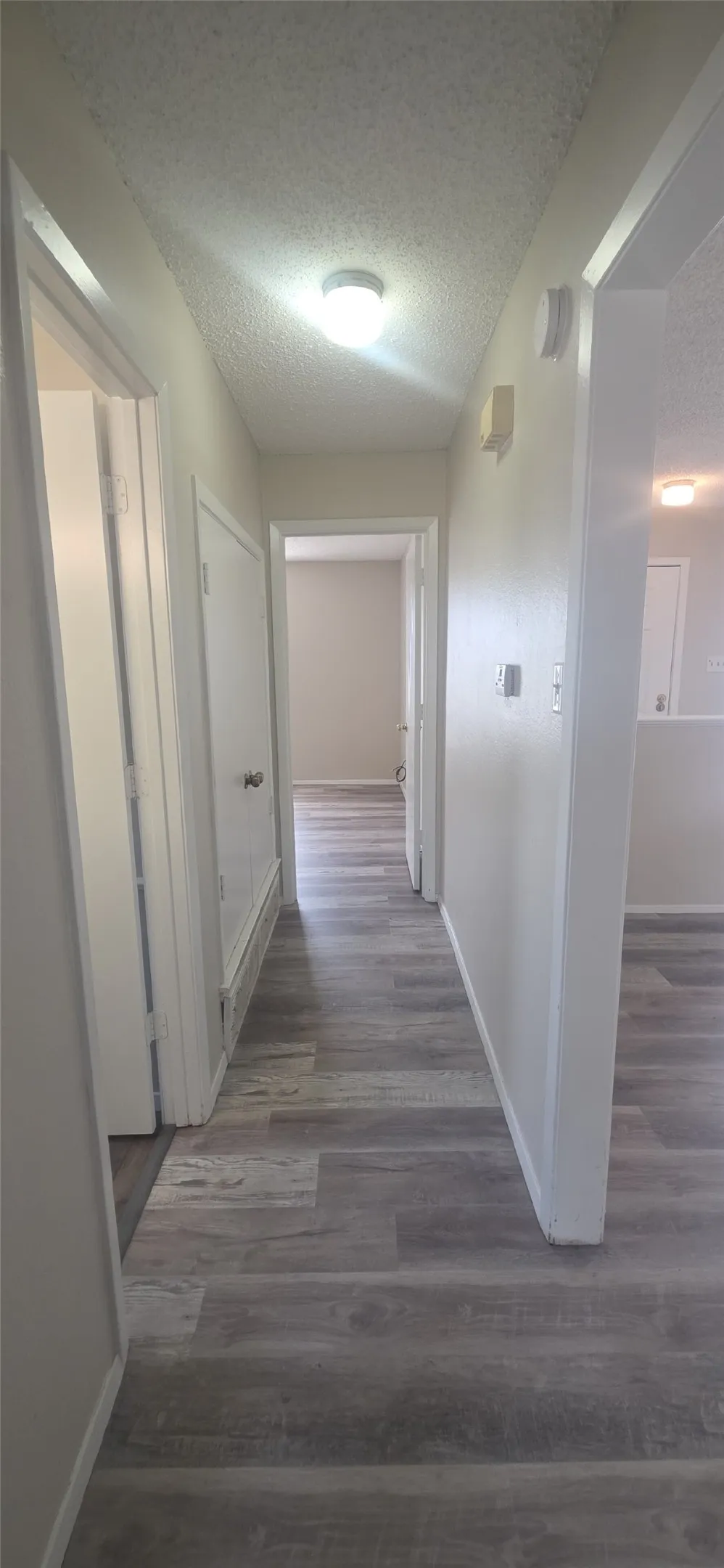 Hallway featuring wood-finish flooring, light neutral paint, and overhead lighting
