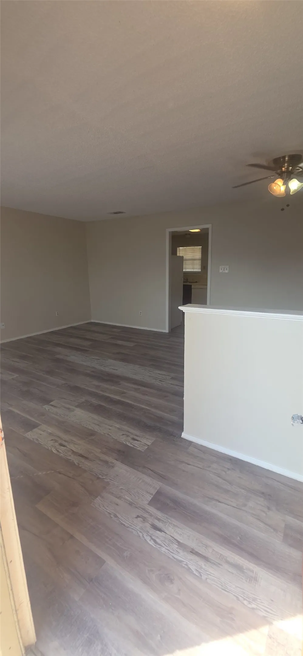 Spacious room featuring wood-finish flooring, neutral paint, and a ceiling fan