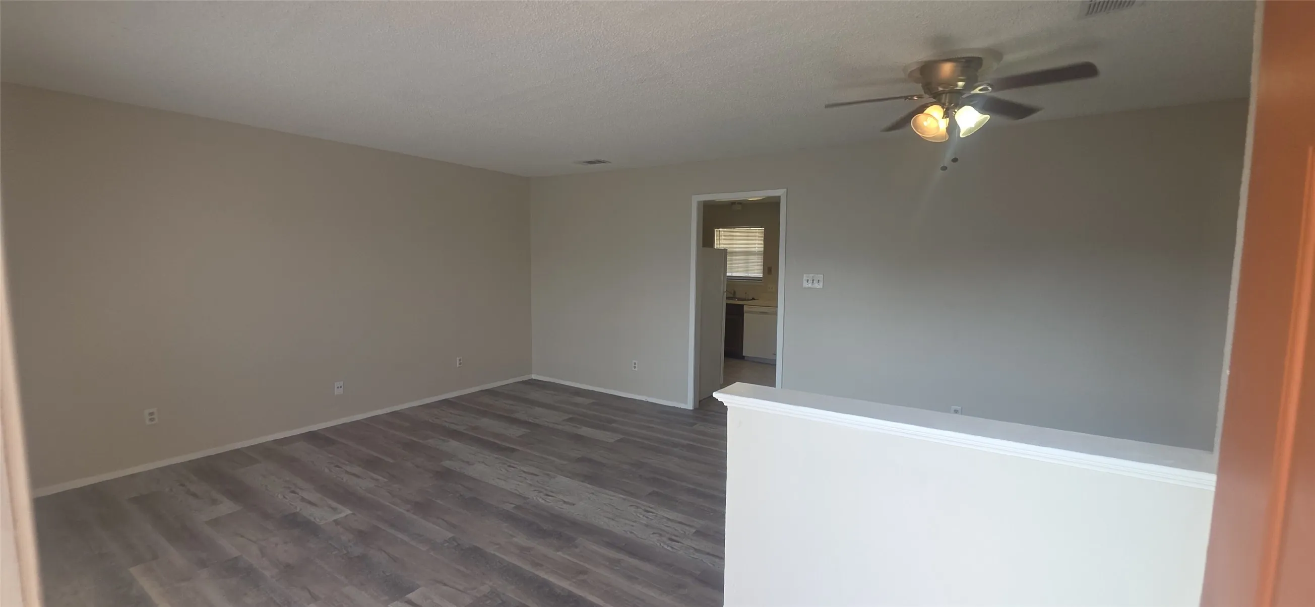 Spacious living area featuring wood-finish flooring, neutral wall tones, and a ceiling fan with integrated lighting