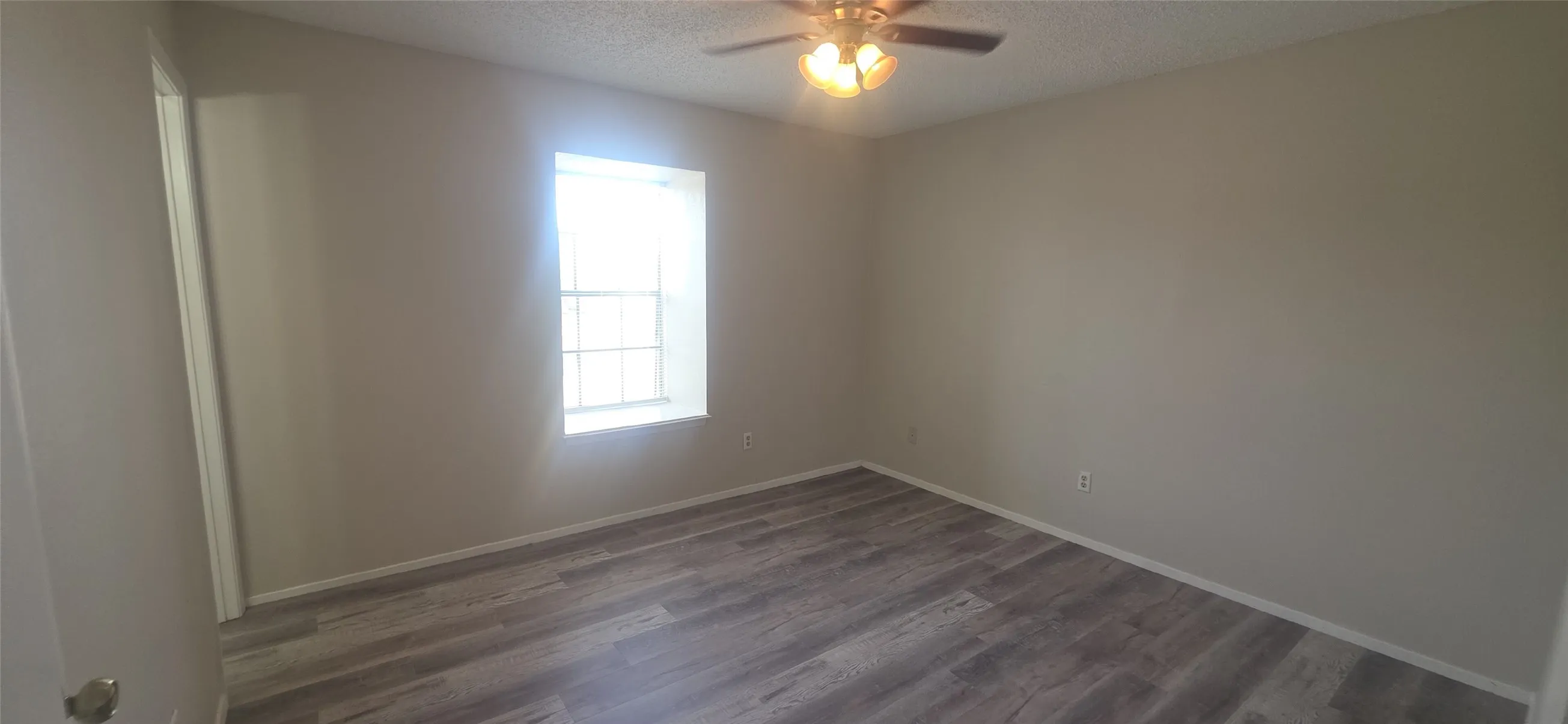 Wood-finish flooring, neutral wall tones, ceiling fan with integrated lighting, and a single pane window