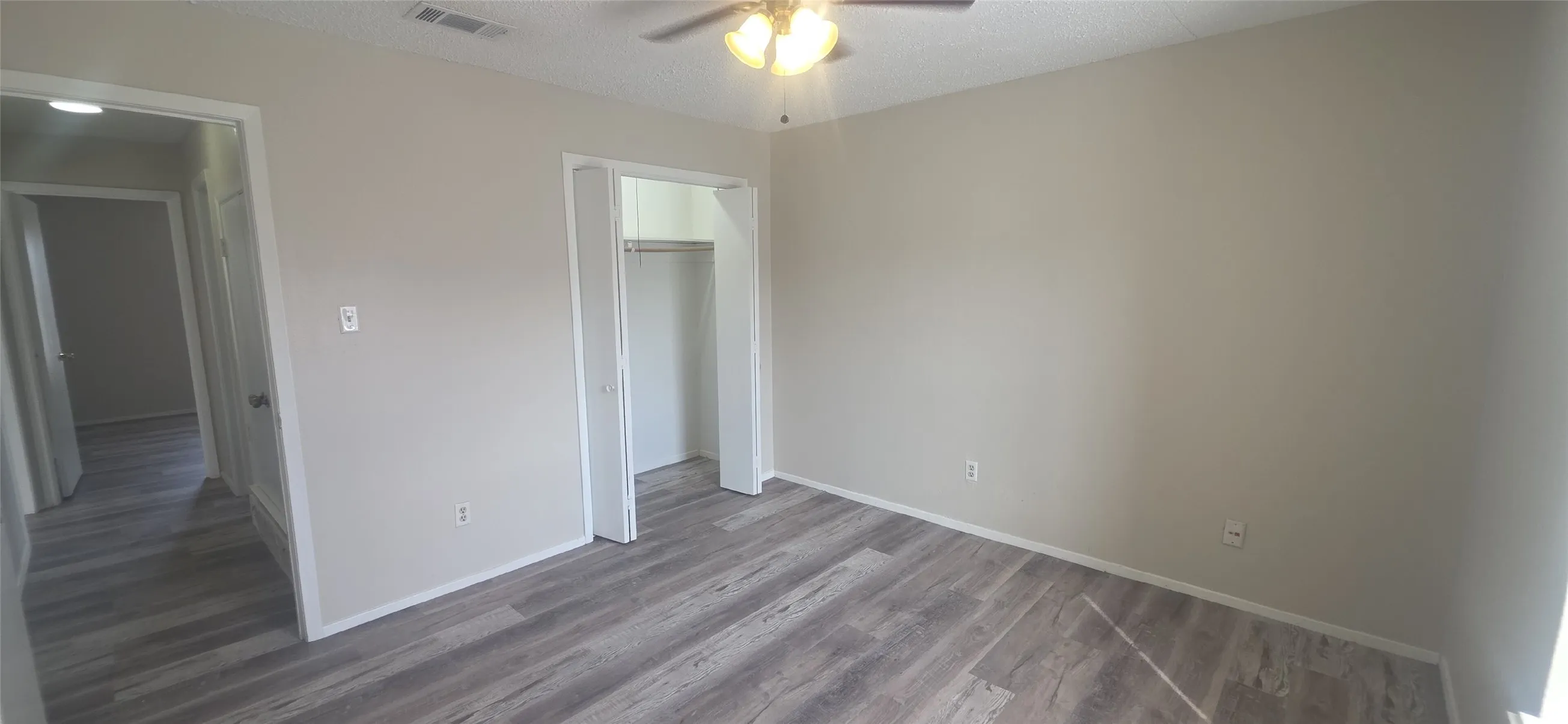 Wood-finish flooring, neutral wall tones, ceiling fan with integrated lighting, bi-fold closet doors, and recessed ceiling vent