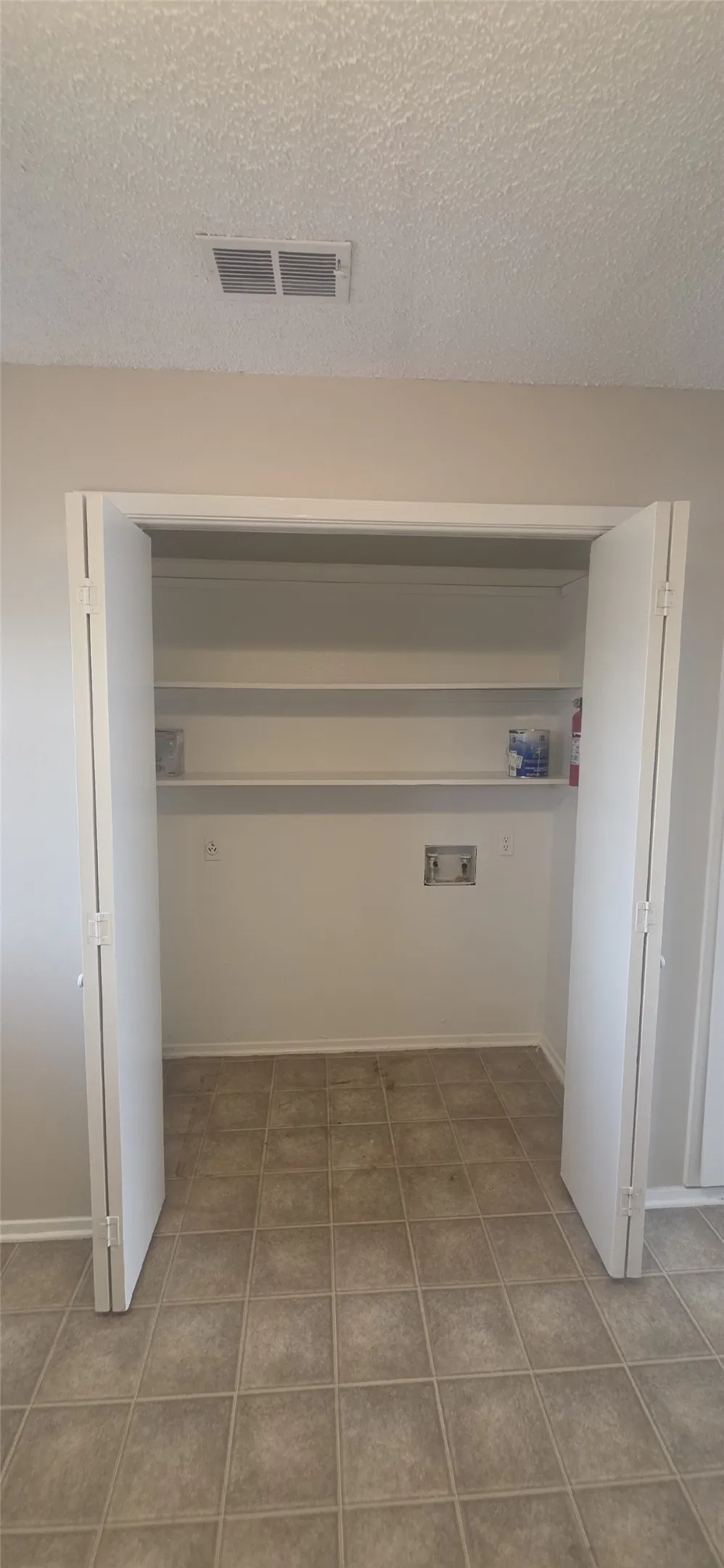 Laundry area with bi-fold doors, two built-in shelves, and a tiled floor