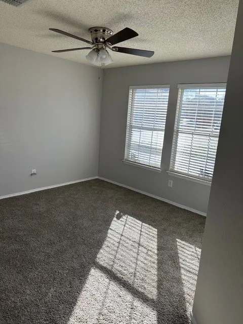 Two windows with horizontal blinds, overhead ceiling fan with light fixture, light gray wall finish, and gray carpeting
