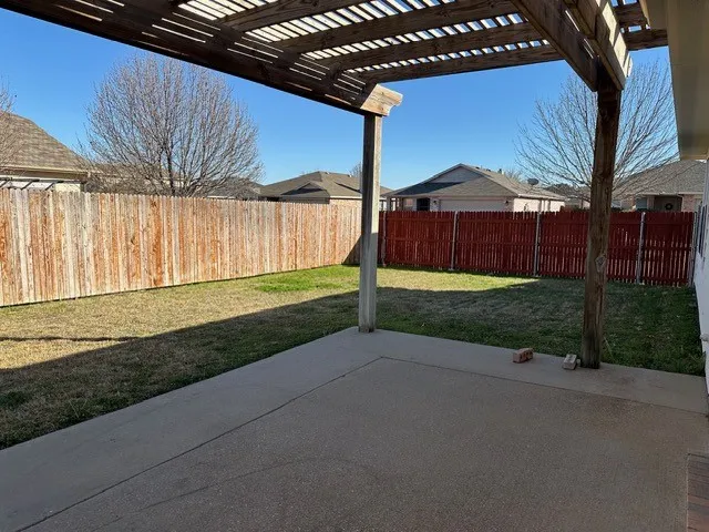 Concrete patio with an overhead wood pergola, enclosed by a wood privacy fence