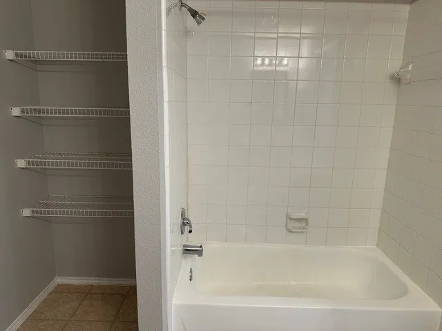 White ceramic tile shower surround with a built-in tub, chrome showerhead, and faucet
