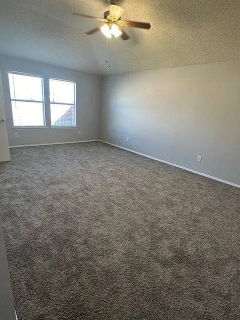 Spacious room featuring neutral carpeting, light gray walls, a multi-pane window, and a ceiling fan with integrated lighting