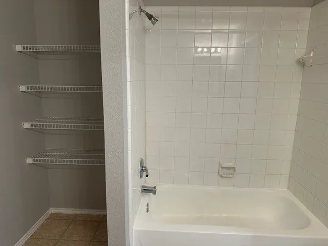 White tiled bath with shower fixture, and a built-in shelving unit with four wire shelves