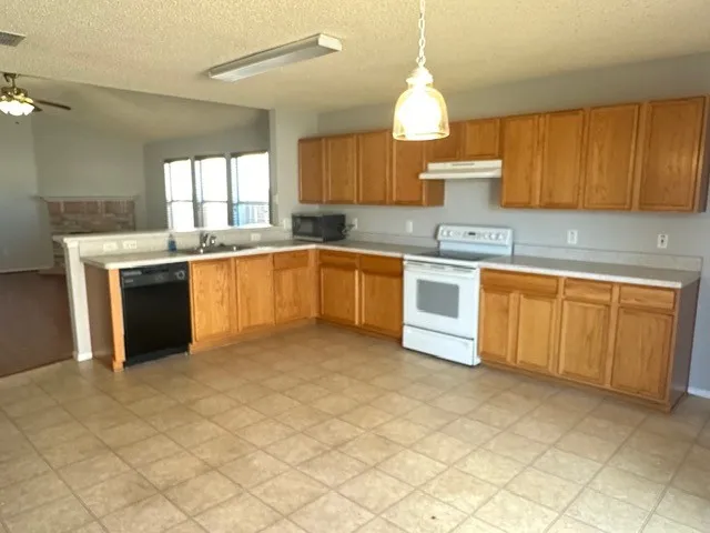 Expansive kitchen featuring wood-finish cabinetry, tile flooring, and integrated white appliances