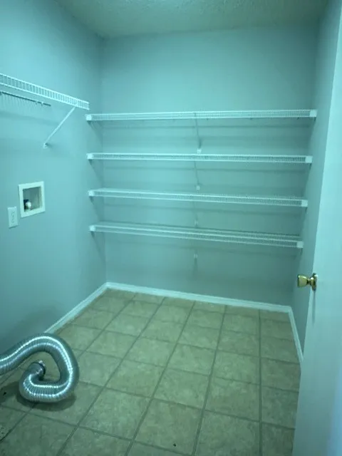 Utility room featuring tile flooring, multiple wire shelving units, and appliance hookups