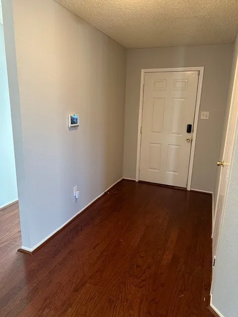Wood-finish flooring throughout, white paneled door, and neutral wall paint