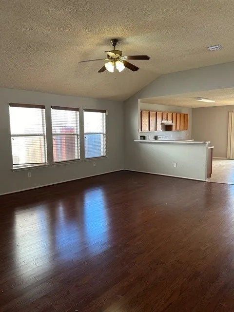 Vaulted ceiling with a ceiling fan, multiple windows with blinds, wood-finish flooring, and a breakfast bar