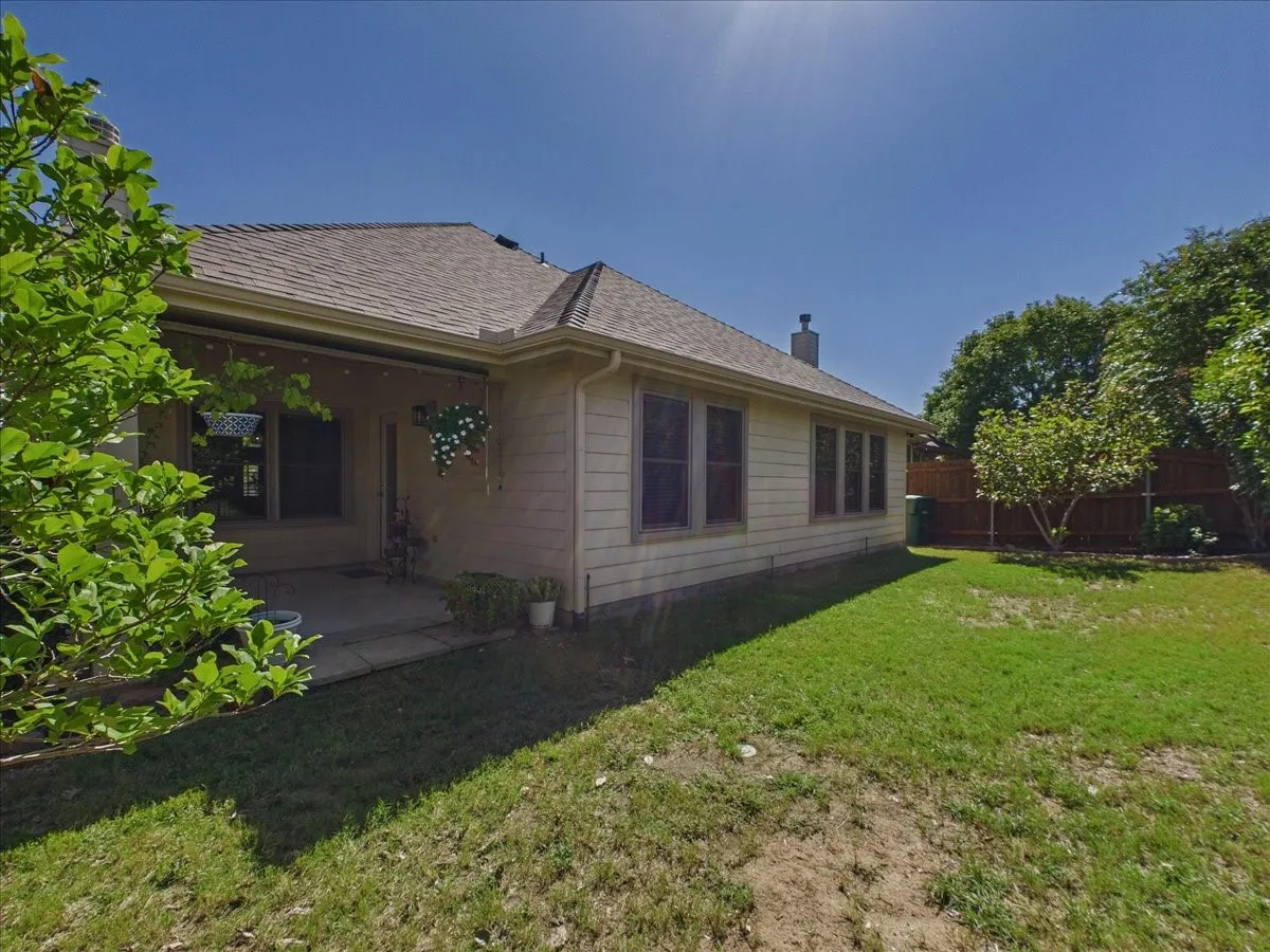 Expansive lawn area with mature trees, covered patio, and a privacy fence