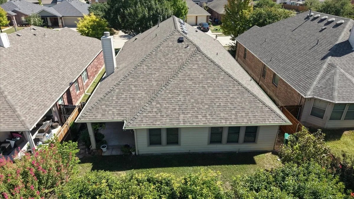 Architectural shingle roof, covered patio, multiple windows, established perimeter landscaping, and a fenced property line