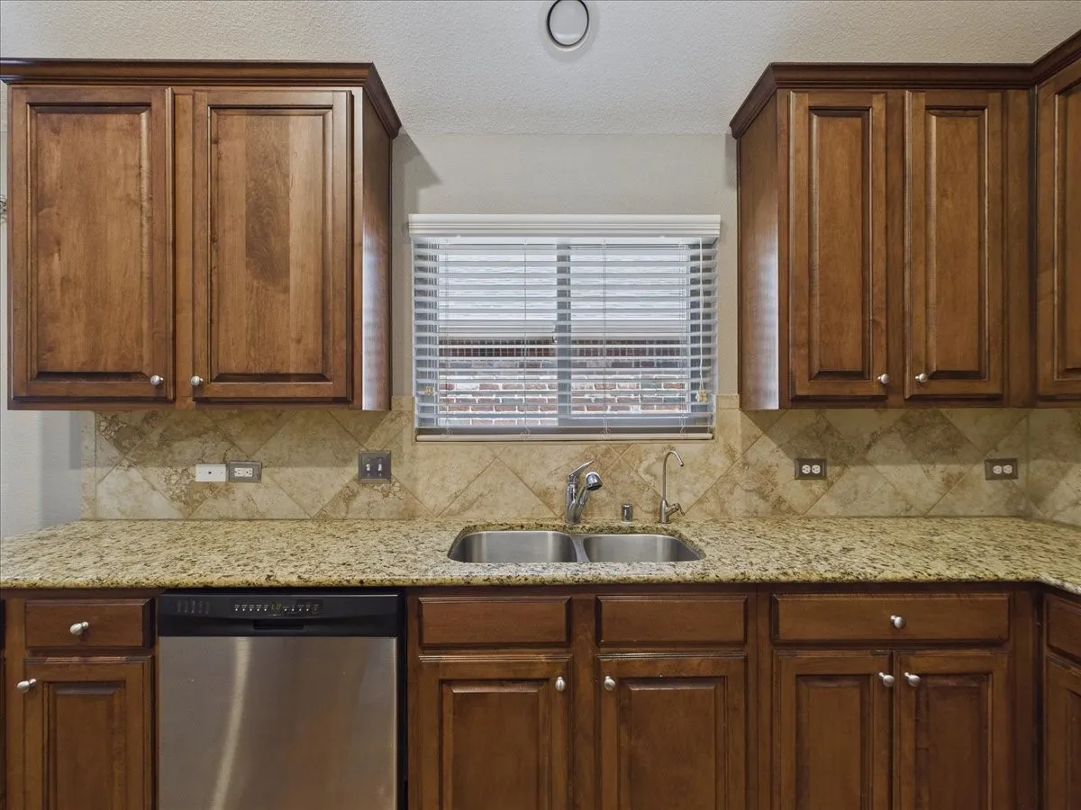 Kitchen featuring wood cabinetry, granite-style countertops, a stainless steel double-basin sink, and a tiled backsplash