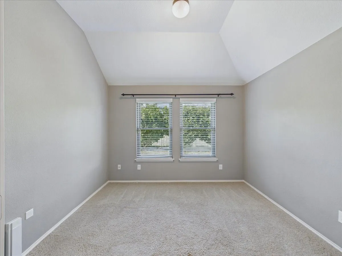 Vaulted ceiling, two windows with blinds, neutral carpet, and recessed lighting