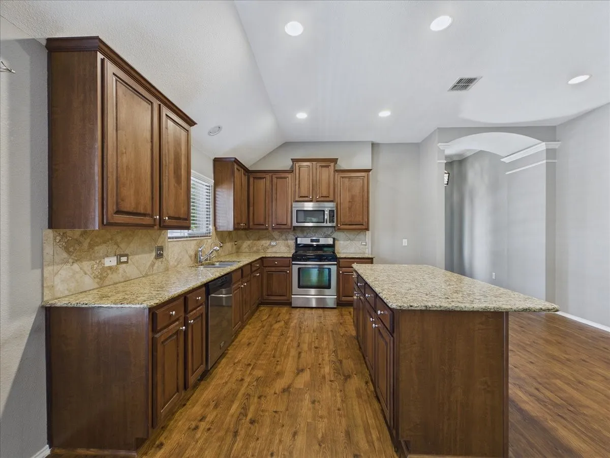 Kitchen featuring wood-finish cabinetry, granite countertops, tile backsplash, stainless steel appliances, and wood-finish flooring
