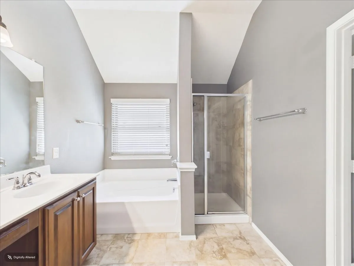 Walk-in shower with clear glass enclosure, a built-in tub, and a vanity with a white countertop and wood-finish cabinetry