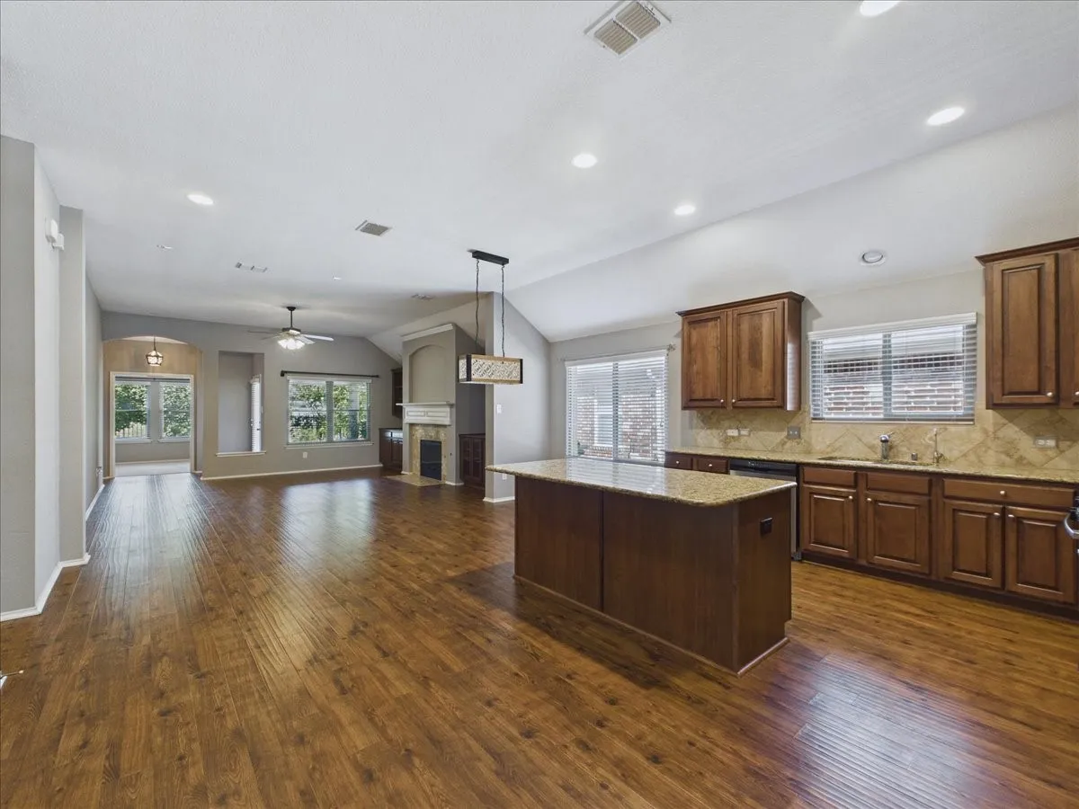 Wood-finish flooring throughout, vaulted ceilings with recessed lighting, kitchen island with stone countertop, wood cabinetry, and a fireplace with a stone surround