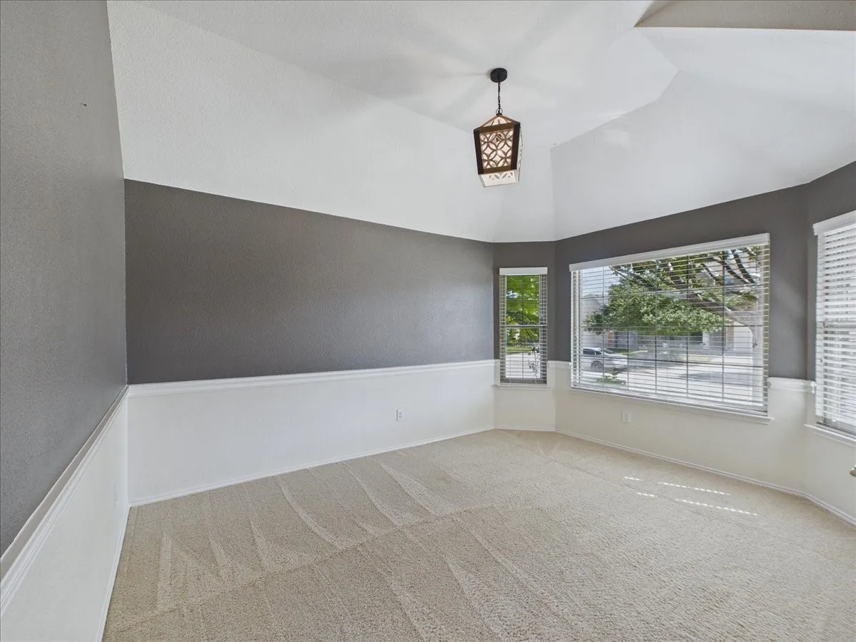 Vaulted ceiling with an ornamental pendant light, large bay window, and a secondary window, featuring two-tone walls with wainscoting and carpeting