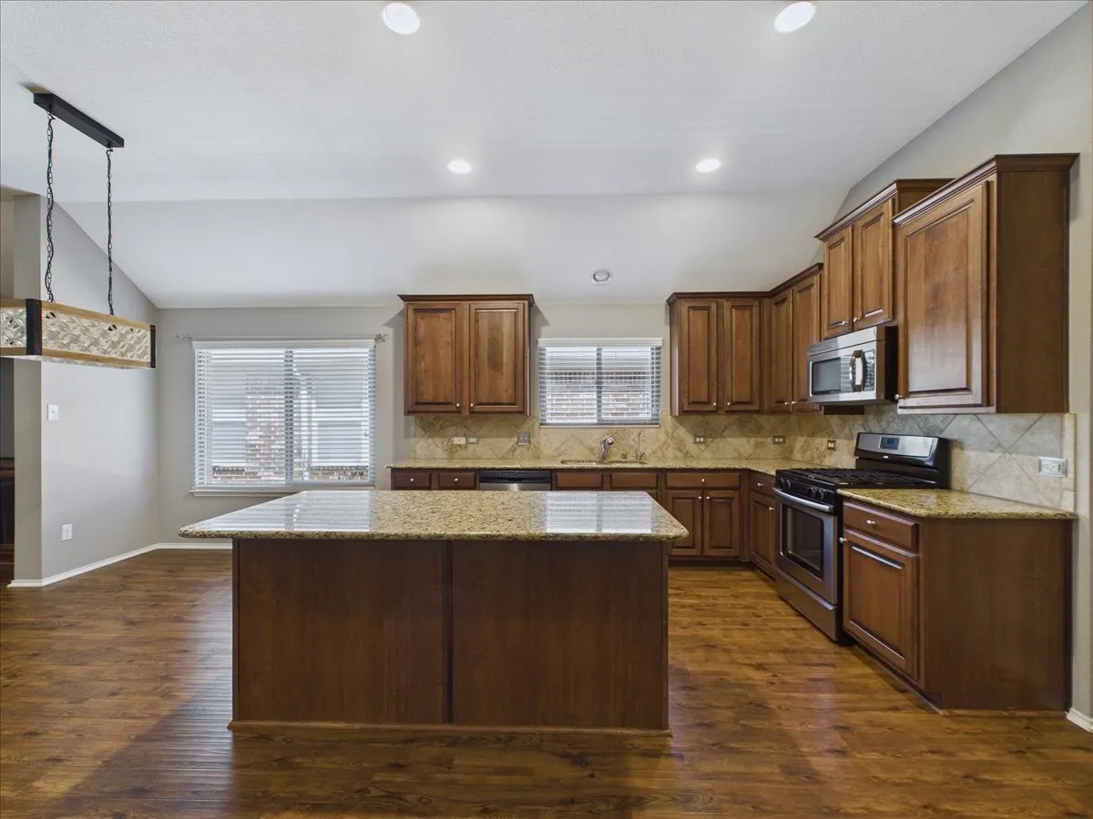 Kitchen featuring wood-finish flooring, a central island with a stone countertop, stained wood cabinetry, stainless steel appliances, and recessed lighting