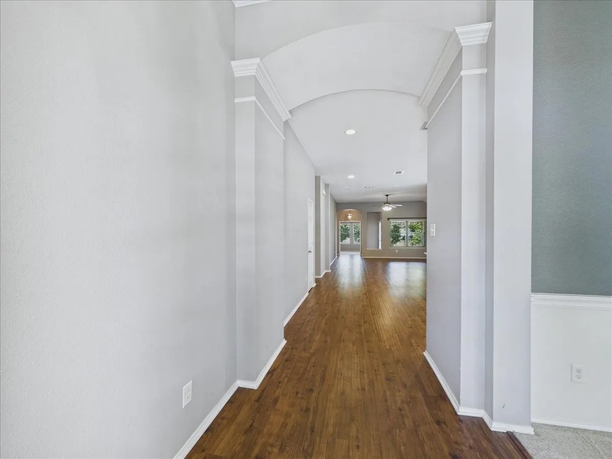 Hallway with wood-finish flooring, an arched entryway, recessed lighting, crown molding, and wainscoting