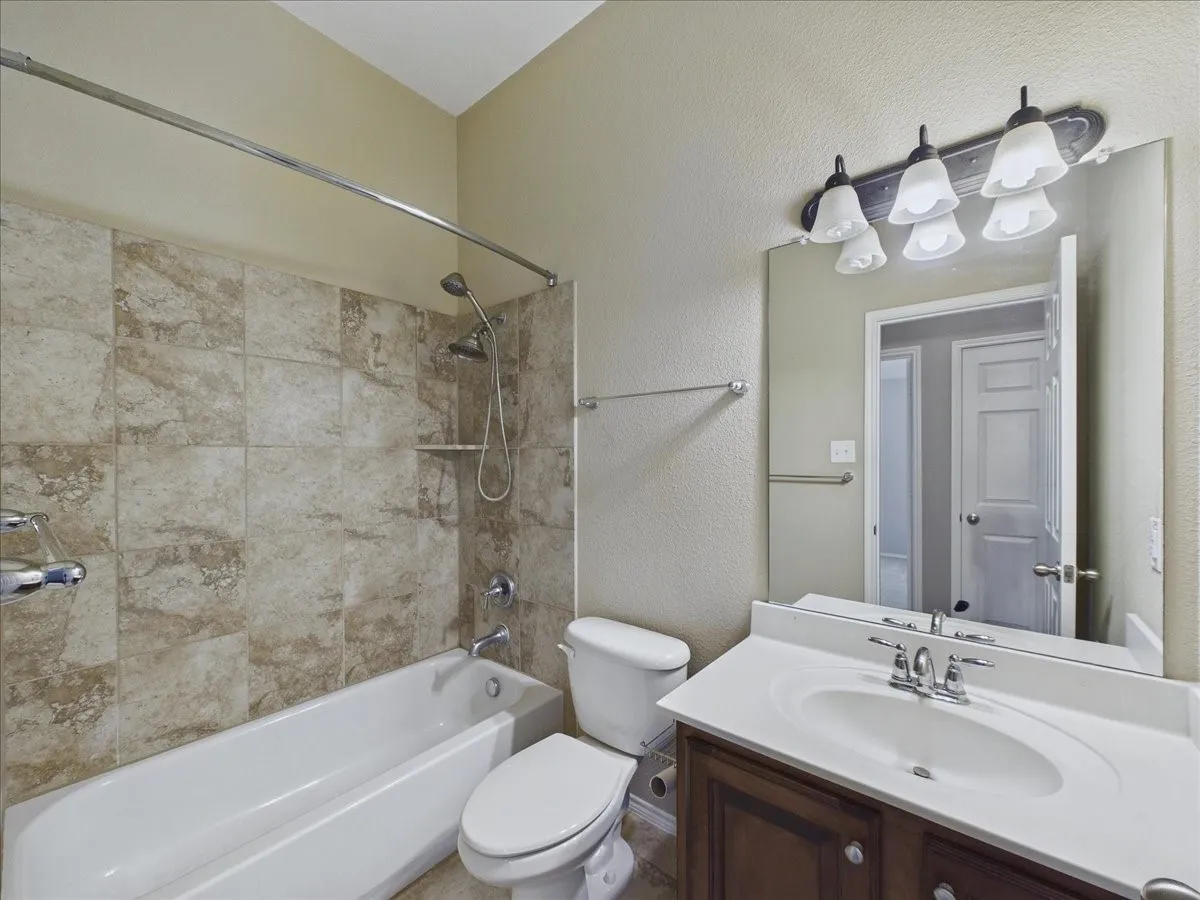 Bathroom featuring a built-in tub with tile surround, a dark wood-finish vanity with an integrated sink, a large wall-mounted mirror, and a multi-bulb vanity light fixture