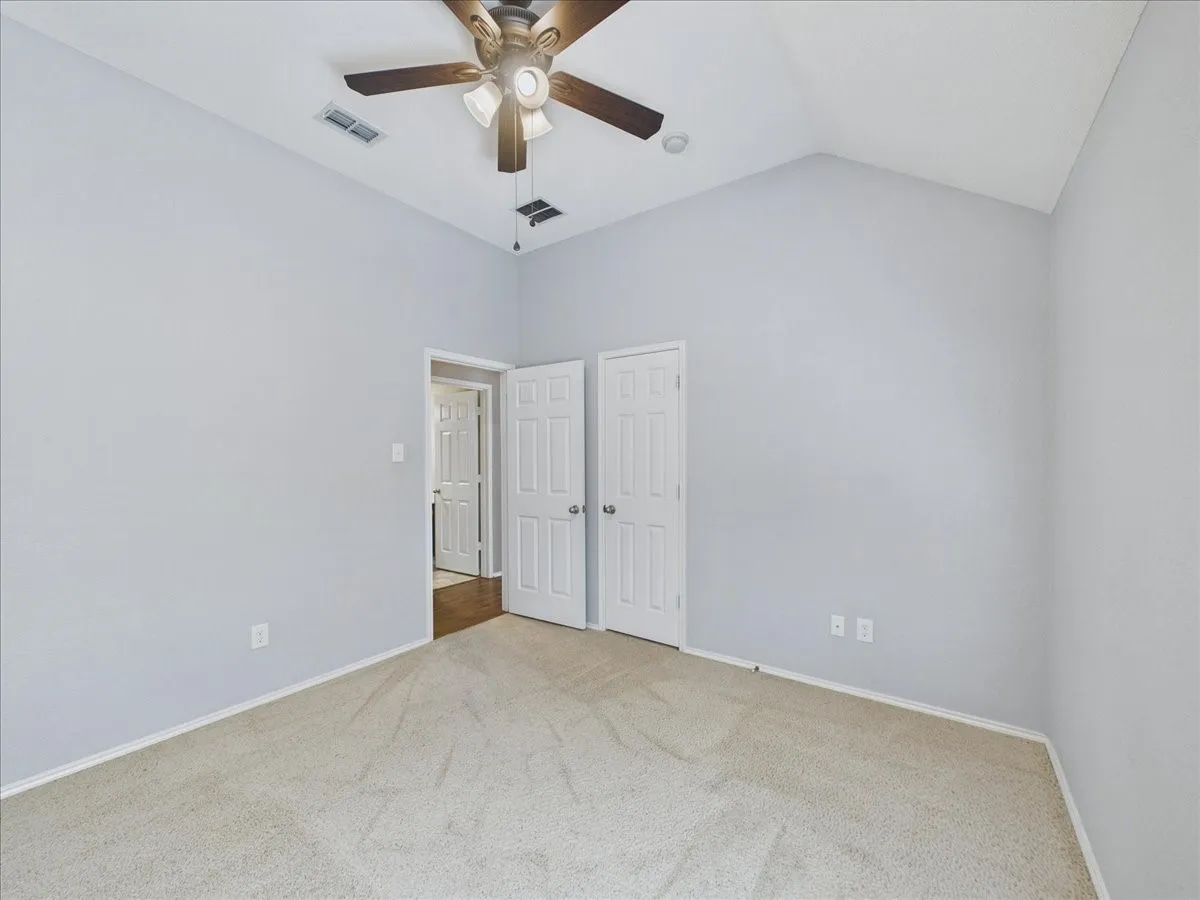 Vaulted ceiling with a ceiling fan, carpeted flooring, and paneled doors