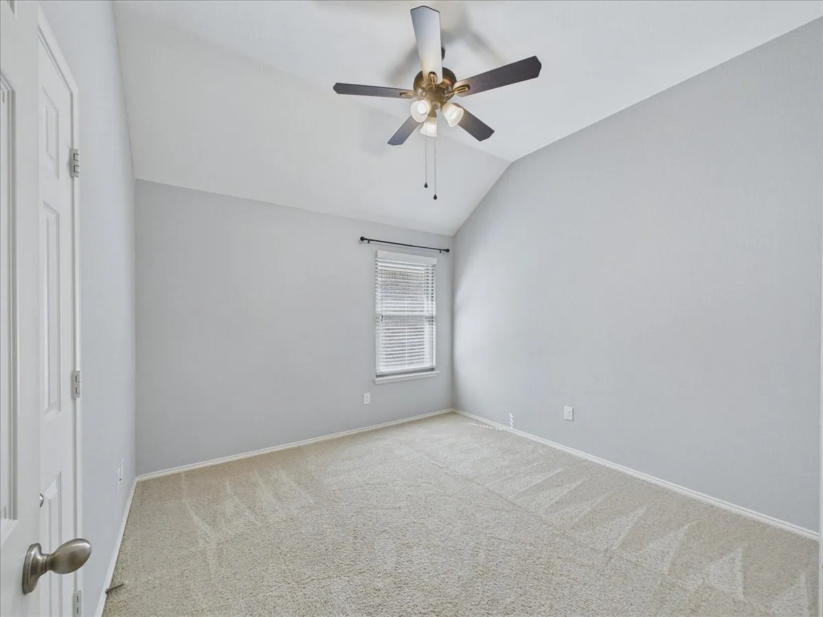 Vaulted ceiling, ceiling fan with integrated lighting, neutral wall finishes, light-colored carpeting, and window with blinds
