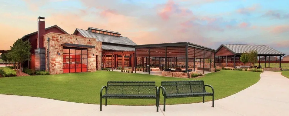 Manicured lawn with a paved pathway, stone and wood-clad building, covered outdoor seating area, and additional covered structure